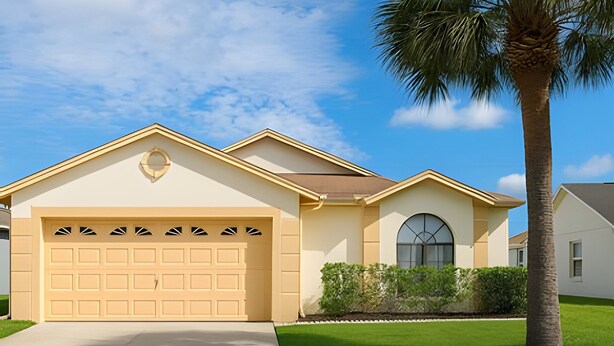 A single-story house with a beige garage door, a small circular window above the garage, and a palm tree to the right. - Prime Location! 3bd/2ba Villa (Kissimmee)