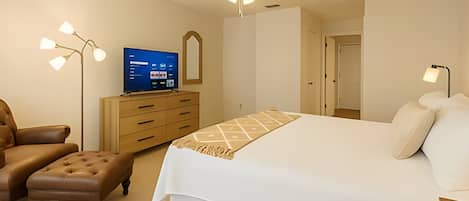 A bedroom with a bed, a desk, a chair, a television, and a ceiling fan.