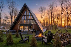 A modern A-frame cabin with a fire pit, outdoor seating, and a view of the sunset.