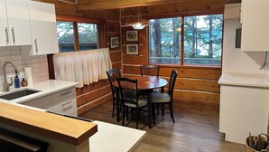 A wooden cabin-style kitchen with a dining table and chairs, a sink, and a sign that reads "We Make You Kindly Welcome". - Welcome to Cloud 99! Cabin has privacy, quiet, awesome view! Recently updated. (Mayne Island)