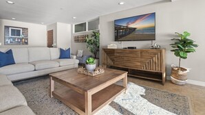 Een moderne woonkamer met een bank, salontafel, televisie en decoratieve planten.