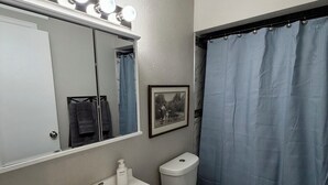 A bathroom with a white sink, a toilet, a shower curtain, and a mirror with lights. - Workman’s Rest Pt. 2 – Quiet Upstairs 2BR for Working Travelers (Gillette)