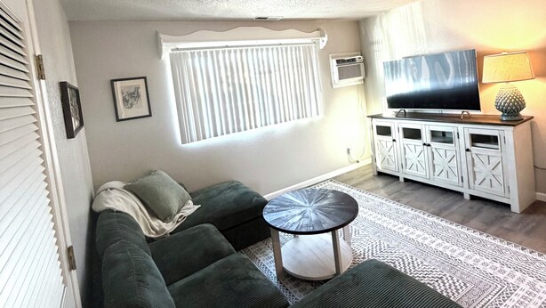 A living room with a sectional sofa, a small round coffee table, a TV on a cabinet, and a patterned rug. - Workman’s Rest Pt. 2 – Quiet Upstairs 2BR for Working Travelers (Gillette)