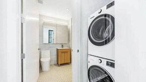 Een moderne badkamer met toilet, wastafel en spiegel. Er staan twee wasmachines boven elkaar.