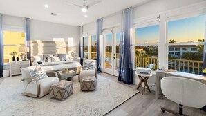A spacious living room with a large sofa set, a coffee table, and a dining area. There is a balcony with a view of the city. - Twin Tides - Bayfront Views + Steps to Bonita Beach (Bonita Springs)