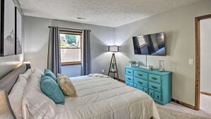 Quarto com cama, cômoda, televisão e janela com cortinas.