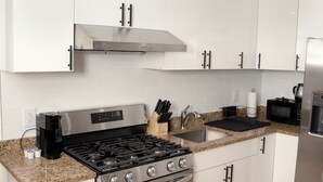 Una cocina moderna con armarios blancos, electrodomésticos de acero inoxidable, encimeras de granito y suelo de madera.
