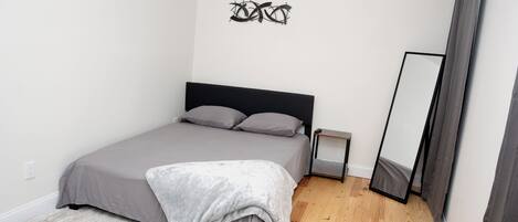 Een slaapkamer met een bed, nachtkastje, spiegel en een kunstwerk aan de muur.