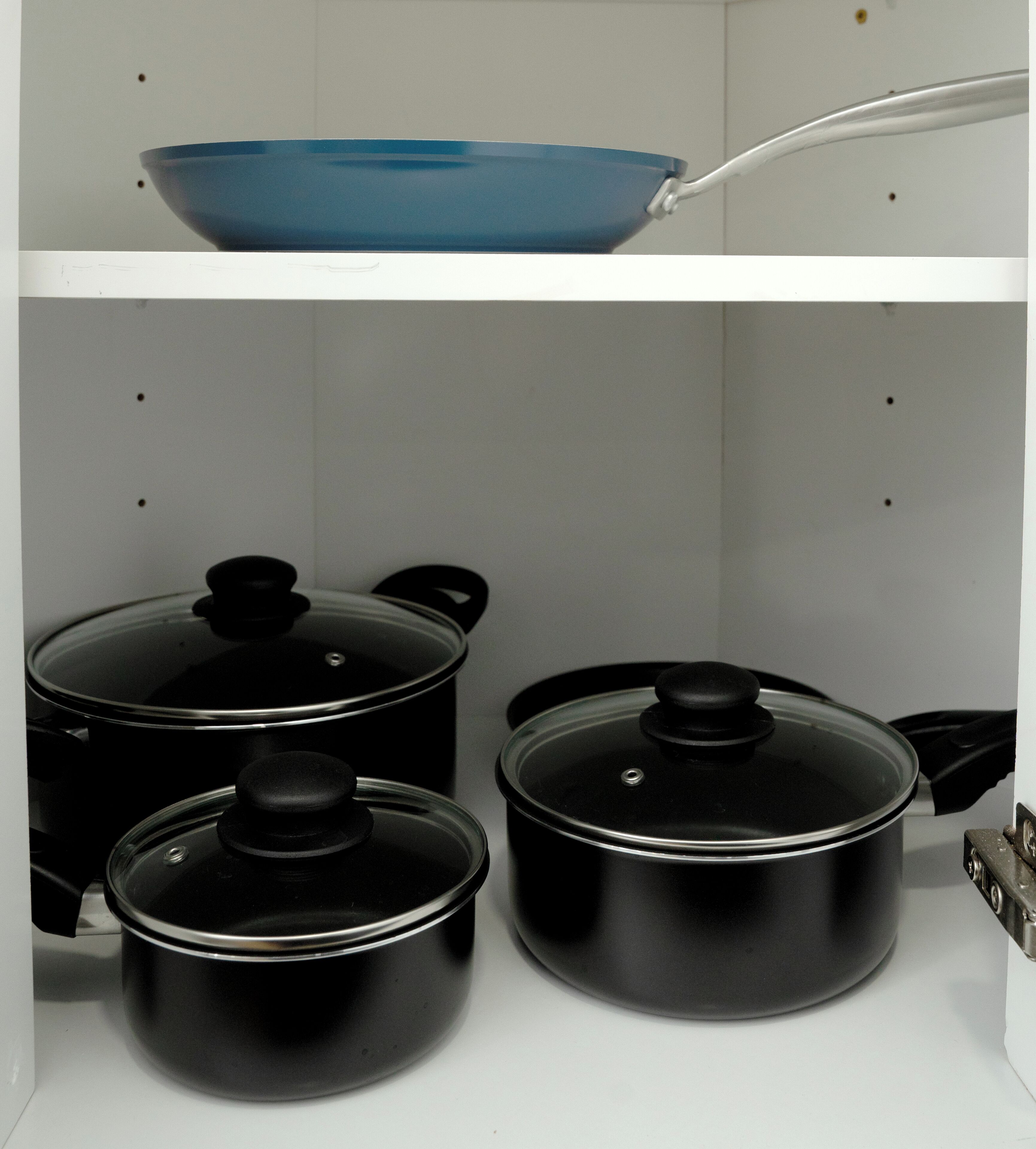 A kitchen with a blue frying pan on a shelf, three black pots with lids, and a stove.