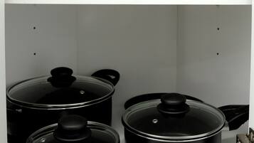 A kitchen with a blue frying pan on a shelf, three black pots with lids, and a stove.