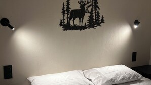 A bed with white bedding, a wall-mounted deer silhouette, and two wall-mounted lights.