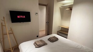 Une chambre à coucher avec un lit, un téléviseur affichant le logo « NETFLIX », une échelle en bois et une armoire avec un miroir.