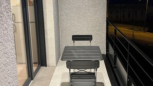An outdoor balcony with a table and chair, a sliding glass door, and a view of the street at night.