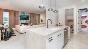 Een moderne keuken met een centraal eiland, een eetgedeelte met tafel en stoelen, en een zithoek met een bank en een televisie.