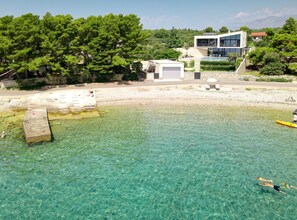 Ein breiter, sauberer Strand mit einem modernen Gebäude, einem Kajak und einer Person, die schwimmt.