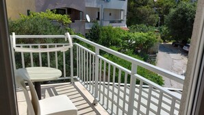 Ein Balkon mit weißem Tisch und Stühlen, einem weißen Geländer und Blick auf umliegende Gebäude und Grünflächen.