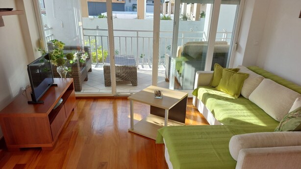 A living room with a wooden floor, a sofa, a TV, and a balcony with outdoor furniture. - Villa Nižić Makarska - One Bedroom Apartment With Balcony (Marina) (Makarska)