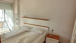 A bedroom with a bed, a bedside table, a lamp, and a window with blinds. - Villa Nižić Makarska - One Bedroom Apartment With Balcony (Marina) (Makarska)
