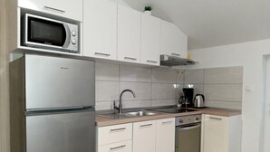 A modern kitchen with white cabinets, a stainless steel refrigerator, a microwave, a sink, a coffee maker, and an oven. - Apartments Tomislav - Two Bedroom Apartment with Terrace and Sea View (Vrsi)