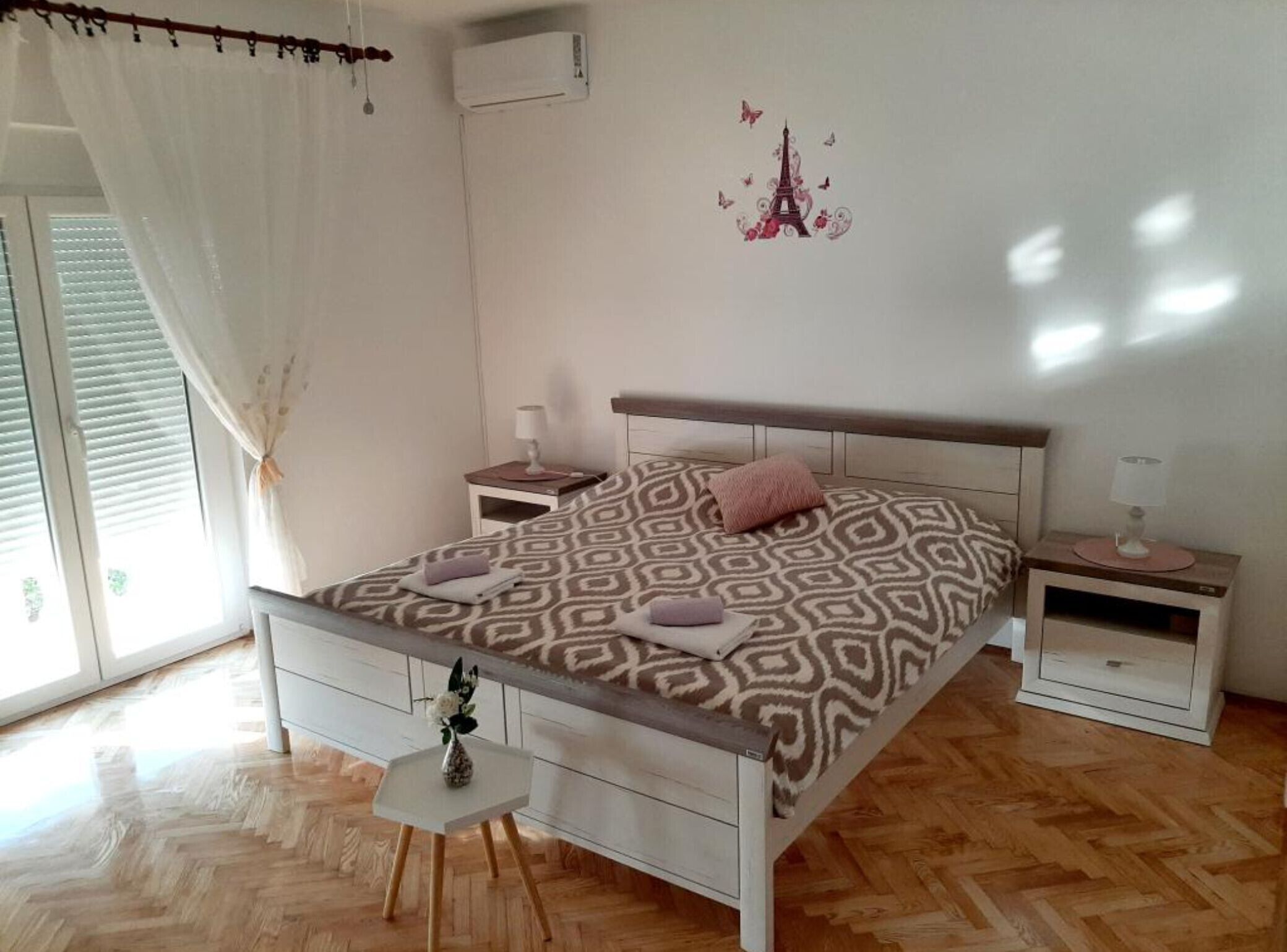 Un dormitorio con cama, dos mesitas de noche, una pequeña mesa blanca y un adorno en la pared.