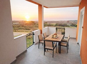 A balcony with a table and chairs, a view of the landscape, and a sunset. - Apartments Tomislav - Superior Two Bedroom Apartment with Terrace and Sea View (Vrsi)