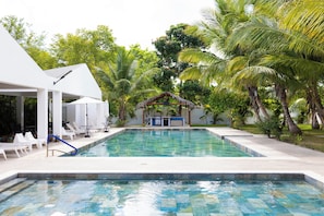 A swimming pool with lounge chairs and a barbecue area surrounded by palm trees. - Punta Cana | 3 Min to Bibijagua Beach | 3 Pools (Punta Cana)