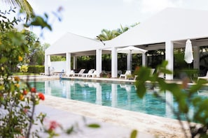 A poolside area with lounge chairs and umbrellas, surrounded by greenery. - Punta Cana | 3 Min to Bibijagua Beach | 3 Pools (Punta Cana)