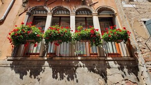 Eine Gebäudefassade mit drei Fenstern, jedes mit einem Balkon, der mit roten Blumen geschmückt ist.