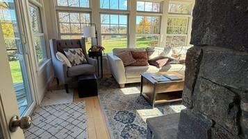 A cozy living room with a stone fireplace, large windows, and a wooden ceiling.