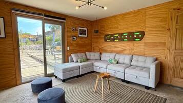 A modern living room with a grey sectional sofa, two round ottomans, a patterned rug, and a unique wall art piece.