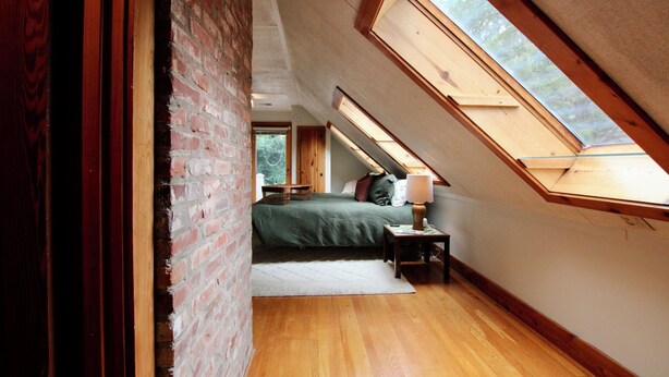 Une chambre avec un plafond en pente, un puits de lumière, un plancher en bois et un lit avec des oreillers et une couverture.