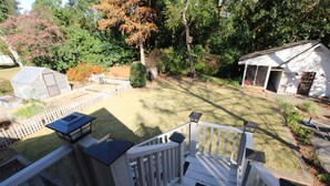 Un jardin avec une terrasse en bois, un petit abri de jardin et une maison.