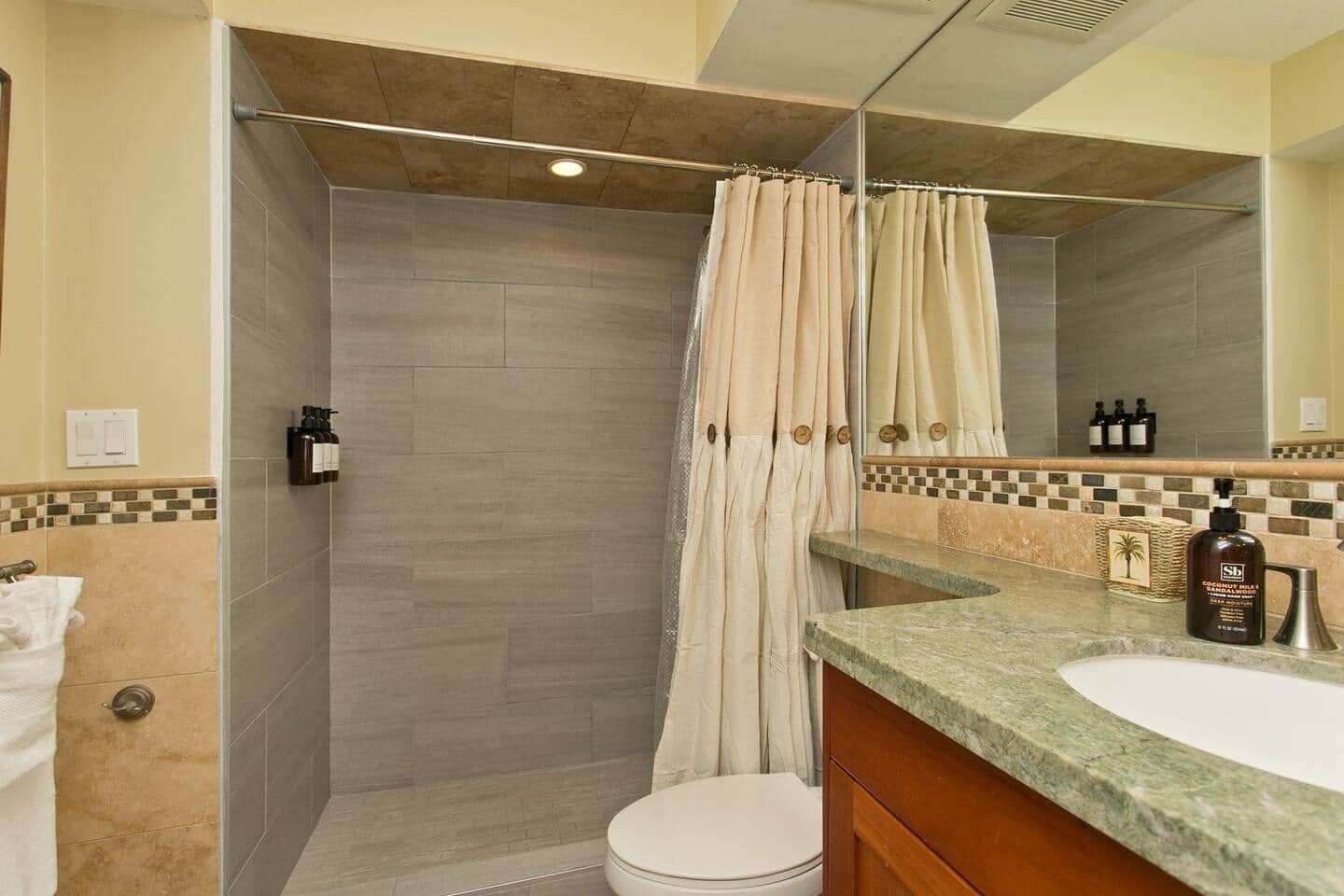 Ein Badezimmer mit Dusche, Toilette, Waschbecken und Spiegel.