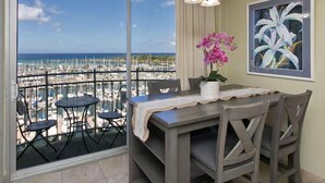 A balcony with a view of a marina, a dining table with chairs, a vase with flowers, and a painting on the wall. - Amazing Ocean Marina View Condo Near Waikiki Beach (Honolulu)