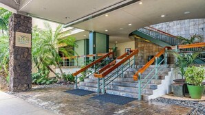A hotel entrance with a stone pillar, a sign, a staircase with wooden railings, and potted plants. - Amazing Ocean Marina View Condo Near Waikiki Beach (Honolulu)