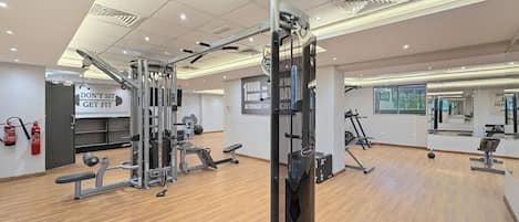 Un gimnasio con diversos equipos de ejercicio, un extintor y un letrero motivacional en la pared.