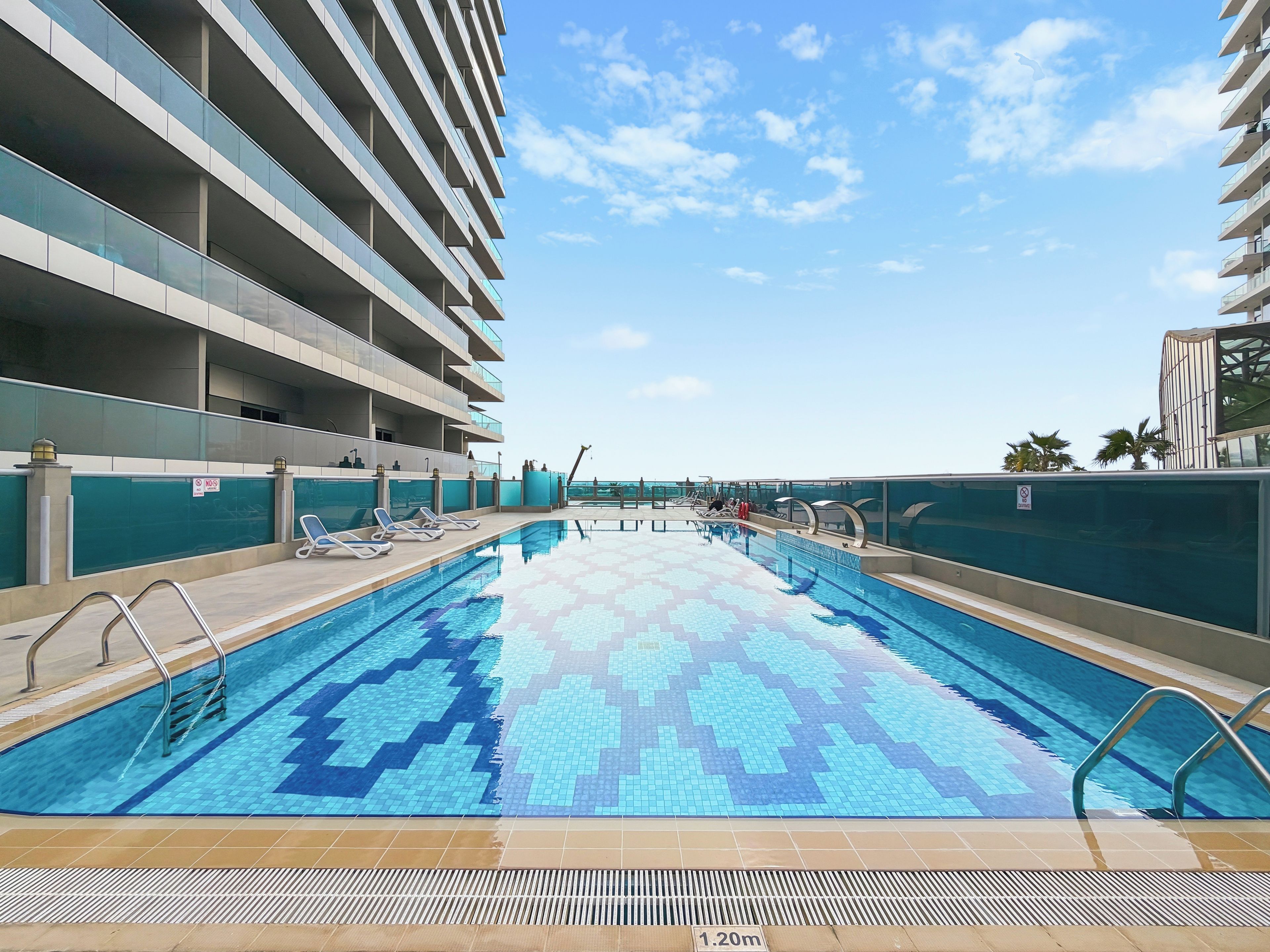 A swimming pool with a tiled pattern, surrounded by a building with multiple balconies.