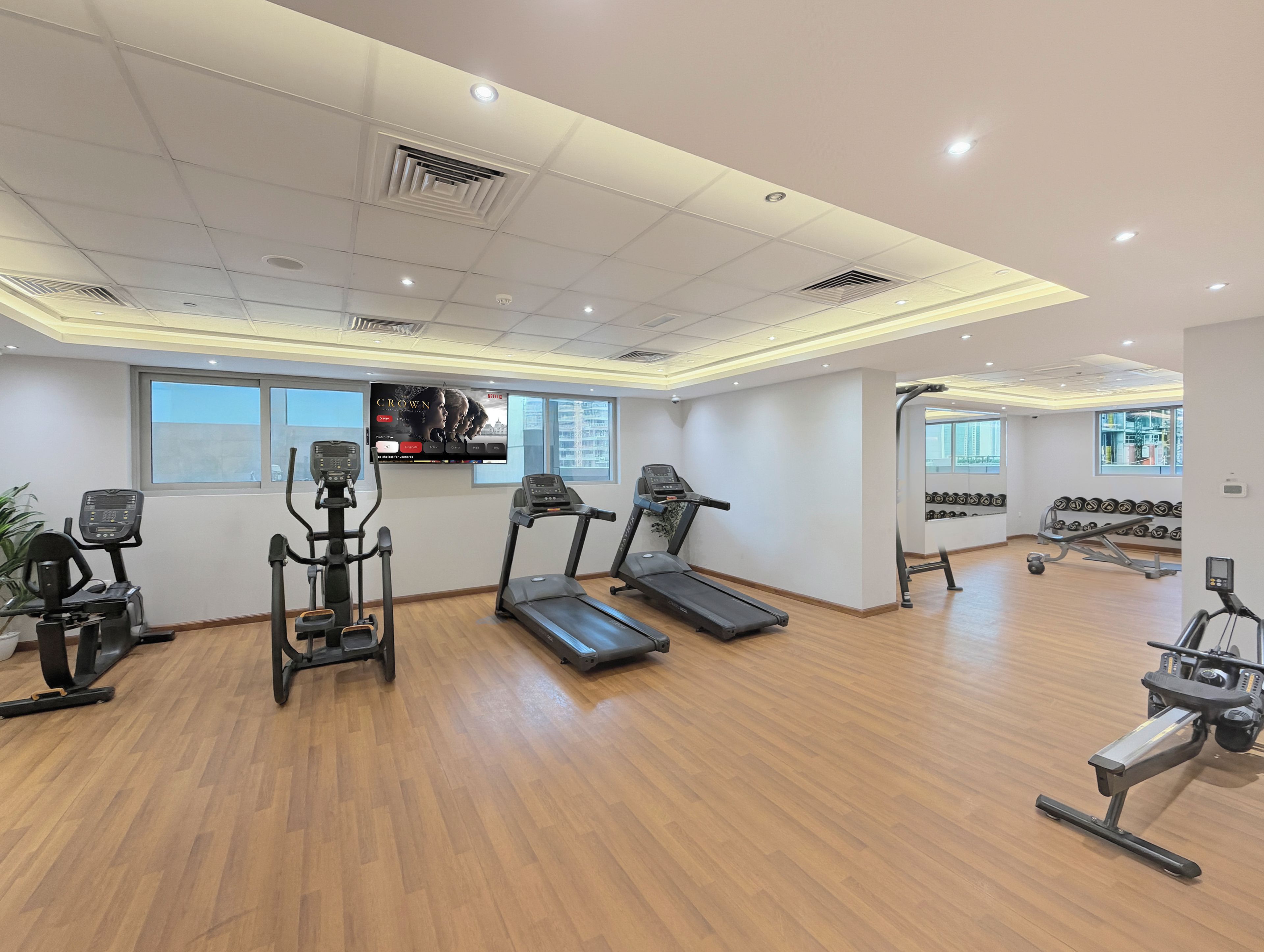 A gym with treadmills, elliptical machines, and a wall-mounted TV.