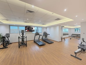 Une salle de sport équipée de tapis de course, de vélos elliptiques et d’un téléviseur fixé au mur.