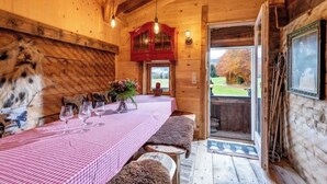 A wooden cabin interior with a dining table set for four, a red cabinet, and a view through the door.