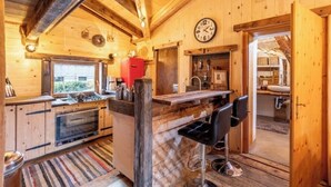 A wooden cabin interior with a kitchen, bar area, and a clock on the wall.