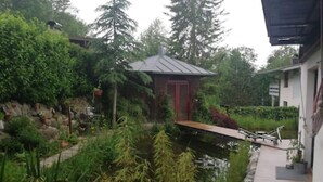A serene garden with a pond, a wooden bridge, and a small building with a red door.
