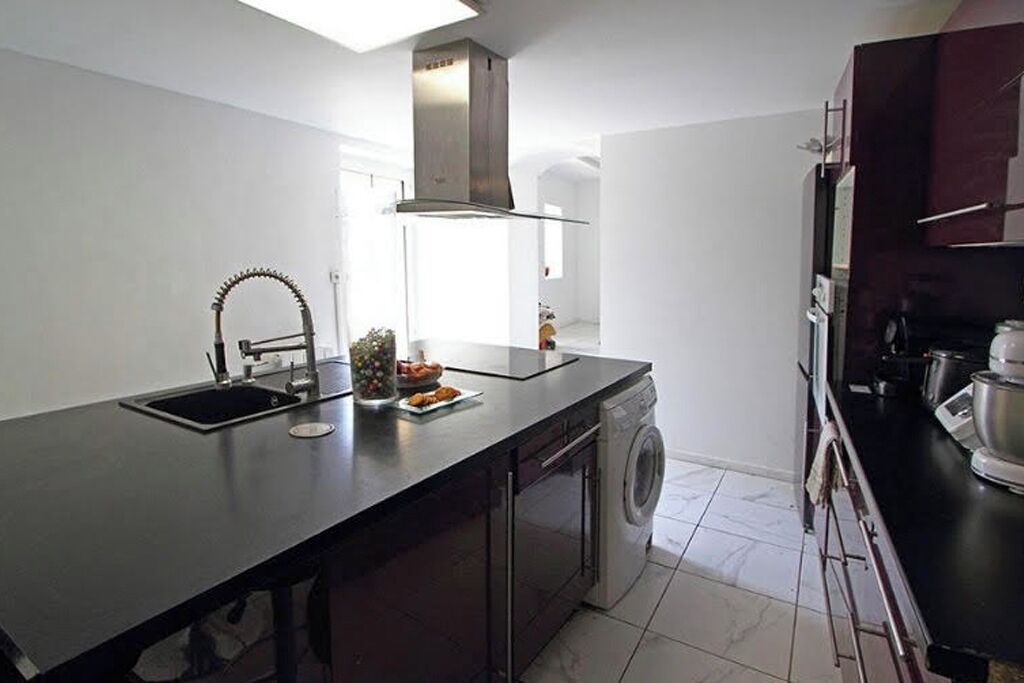 A modern kitchen with a built-in washing machine, a sink, and a stainless steel range hood.