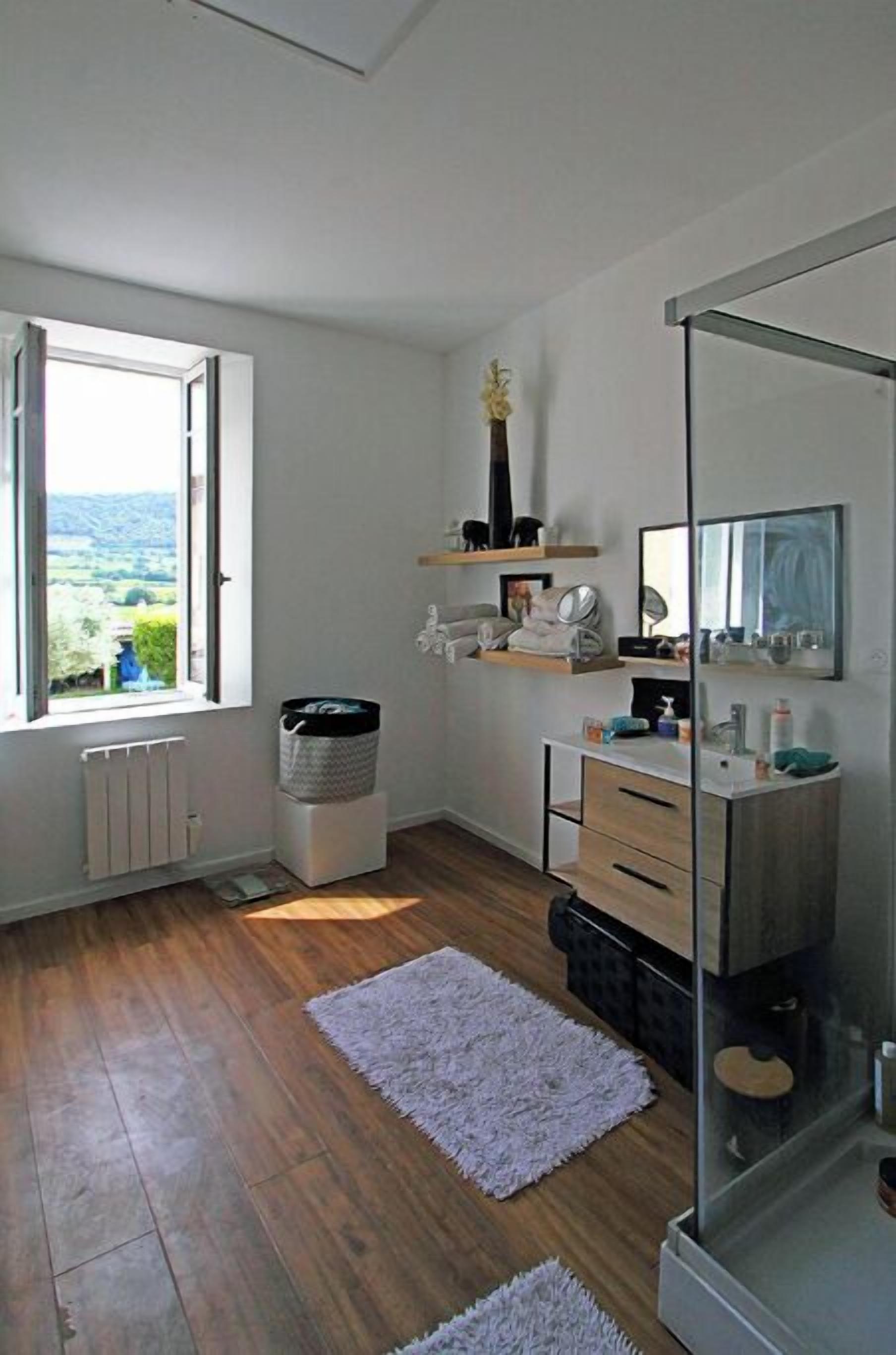A modern bathroom with a large mirror, wooden flooring, a window with a view, and a built-in sink.