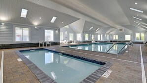 A large indoor swimming pool with multiple lanes, surrounded by lounge chairs and a high ceiling with skylights.