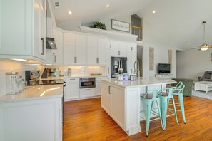 Een moderne keuken met witte kasten, een centraal eiland met barstoelen, een ingebouwde oven en een koelkast.