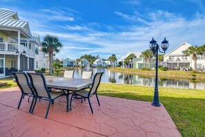 A patio with a table and chairs, a pond, and houses in the background. - Spacious Home w/ Oceanside Village Resort Perks! (Murrells Inlet)