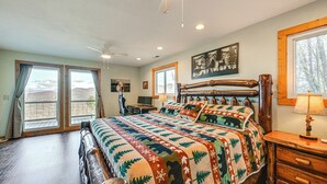 Una camera da letto con un letto grande, una scrivania e una sedia. Sono presenti finestre con tende, una ventola a soffitto e un quadro appeso al muro.