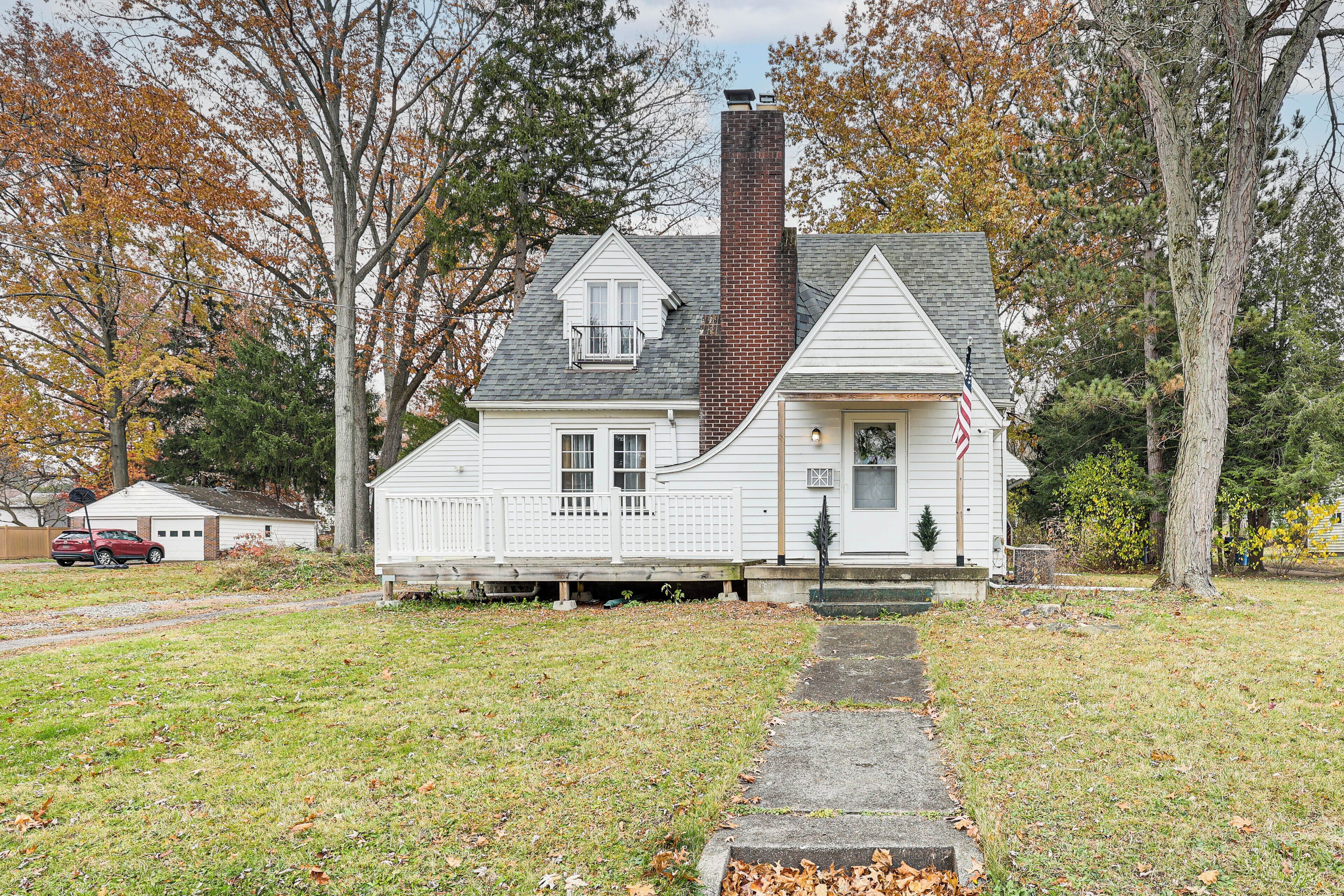 A two-story white house with a brick chimney, a front porch, and a small balcony.