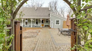 A covered patio area with a brick pathway leading to a wooden deck, surrounded by a wooden fence and a pergola with climbing plants.